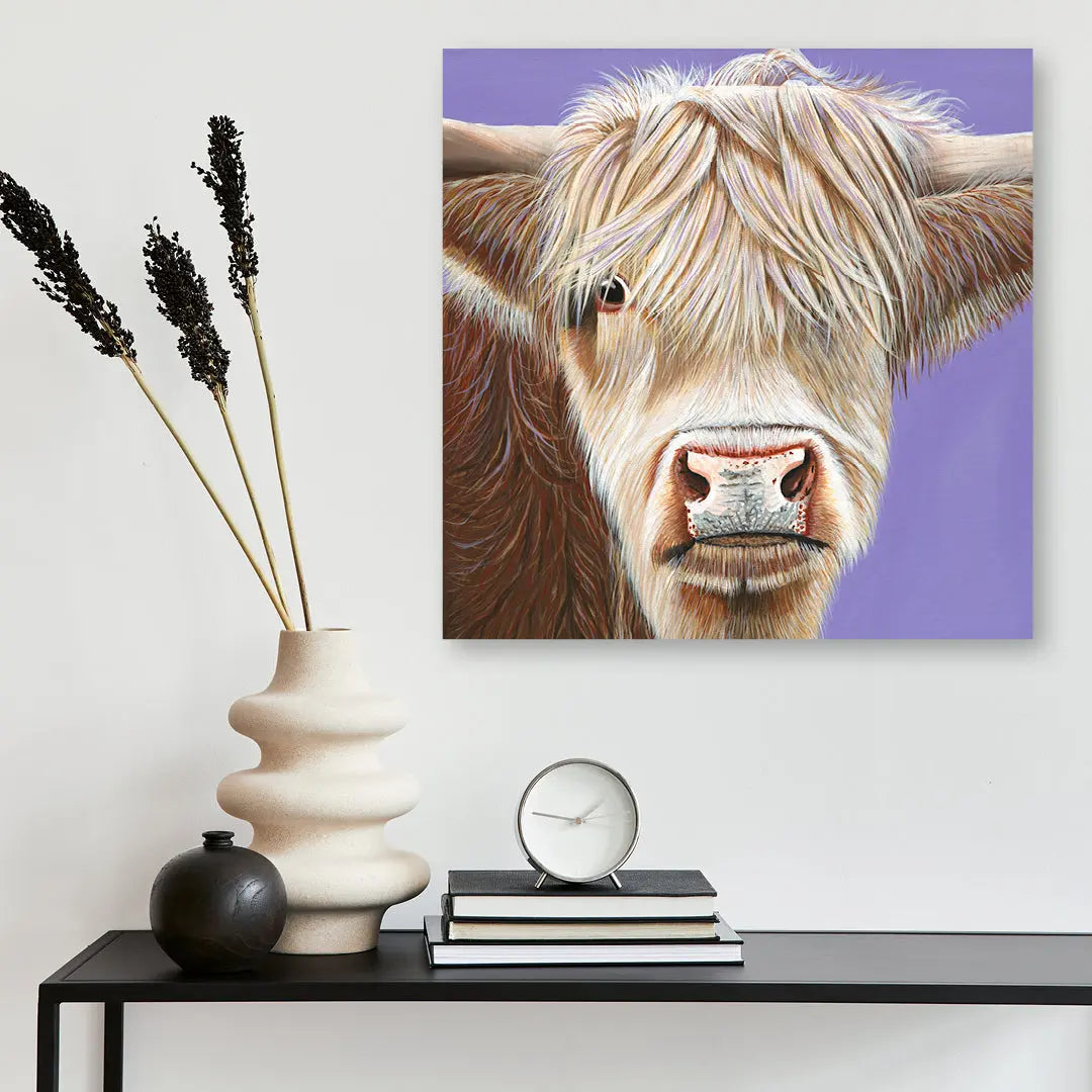 Framed artwork of a Highland cow on a wall above a table with decorative items.