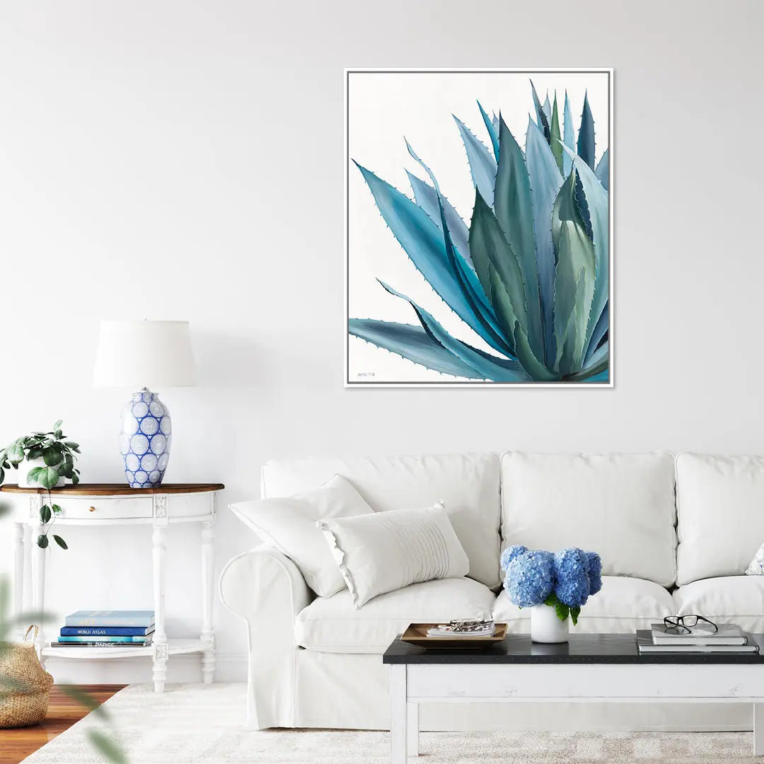Living room with a white sofa, coffee table, and decorative items, featuring a framed artwork of blue agave leaves on the wall.