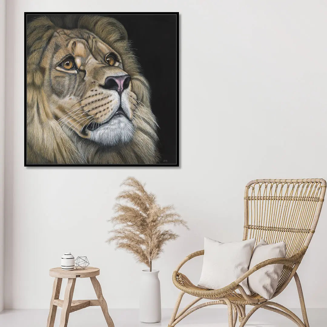 Framed artwork of a lion's head on a wall above a wicker chair and small table.